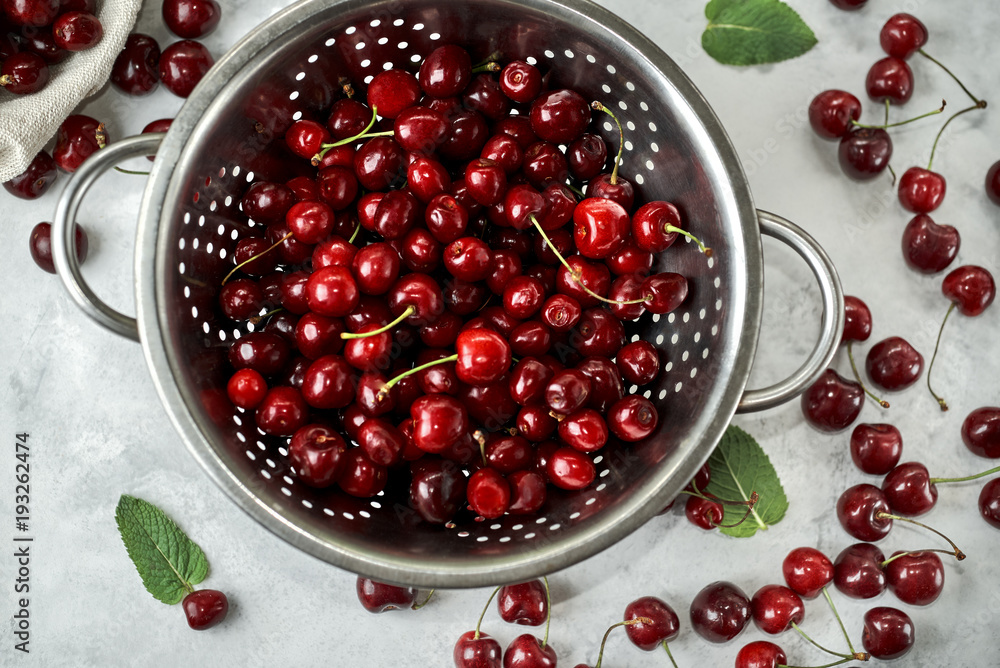 Top view at the colander with ripe cherries. Colander stands on a white surface. Top view at the colander with ripe cherries. Colander stands on a white surface.