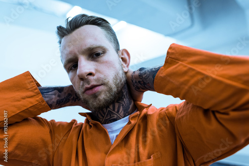 tattooed prisoner with hands behind head looking at camera