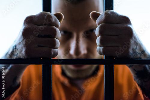 angry prisoner holding prison bars and looking at camera
