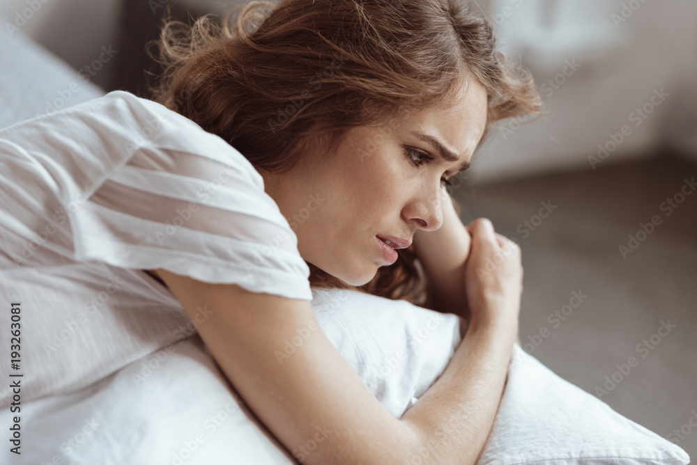 Fototapeta premium What should I do. Worried woman lying on a bed and looking into vacancy while thinking about something serious.