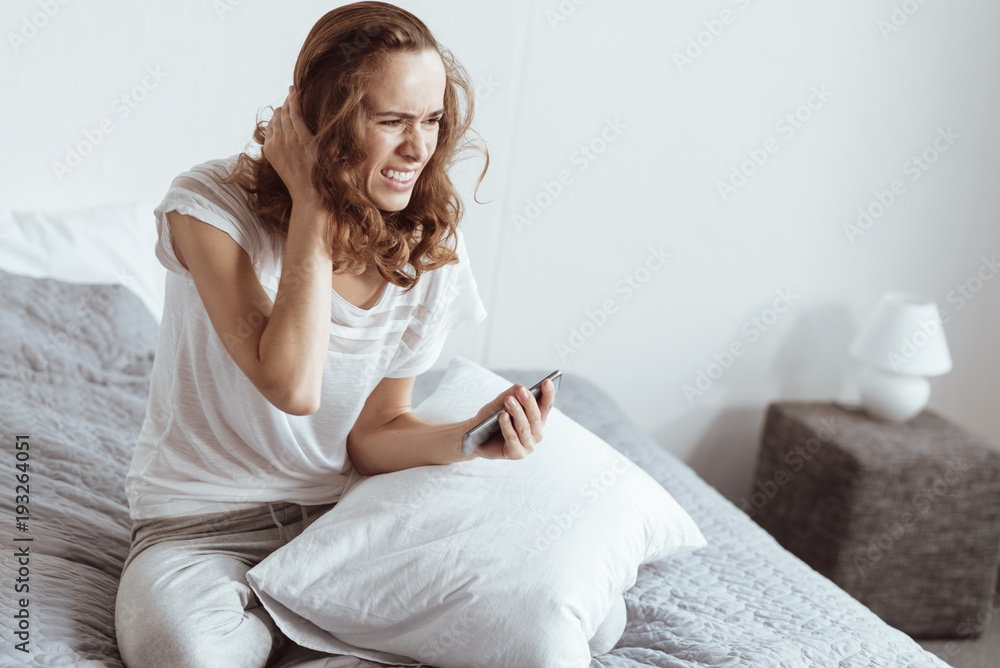 Negative thoughts. Poor stressed lady having a nervous collapse while sitting on a bed and holding her smartphone. Negative thoughts. Poor stressed lady having a nervous collapse while sitting on a bed and holding her smartphone.