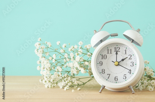 Image of spring Time Change. Summer back concept. Vintage alarm Clock over wooden table.