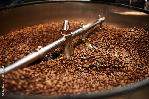 Stainless steel arms mixing freshly roasted coffee beans in large stainless steel cooling drum where the beans are cooled down before packaging or storing them.