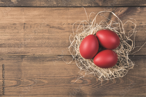 Red easter eggs in nest on wooden background 
