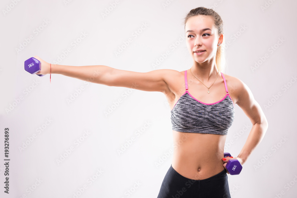 Portrait of young happy smiling woman in sportswear, doing fitness exercise with dumbbells over white background Portrait of young happy smiling woman in sportswear, doing fitness exercise with dumbbells over white background