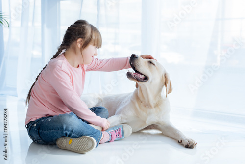 Little girl with down syndrome stroking Labrador retriever head
