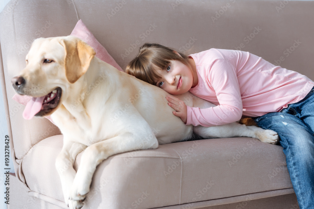 Kid with down syndrome lying on the sofa with Labrador retriever dog Kid with down syndrome lying on the sofa with Labrador retriever dog
