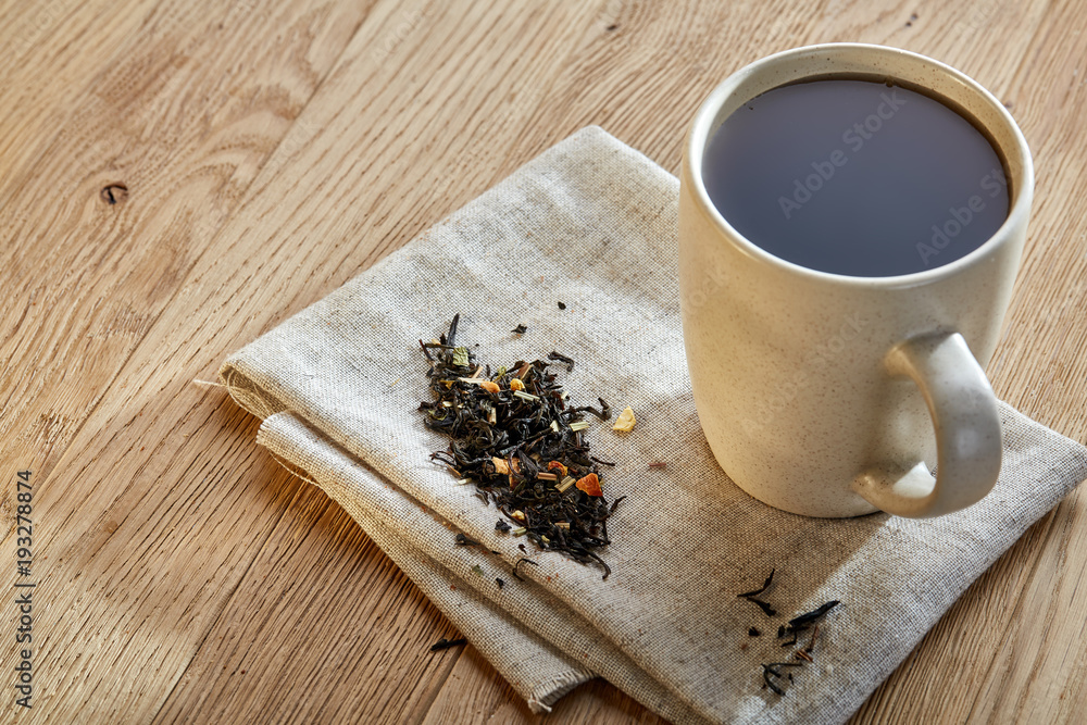 Ceramic cup of tea with scattered tea leaves on a napkin on rustic wooden background, selective focus Ceramic cup of tea with scattered tea leaves on a napkin on rustic wooden background, selective focus