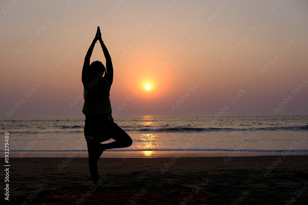 Woman's silhouette doing yoga on the beach at sunset