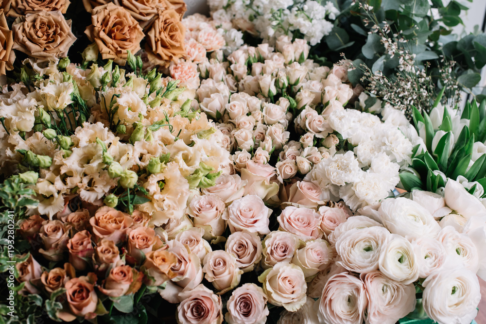 A lot of fresh blossoming flowers (roses, peonies, ranunculus, carnations, eucalyptus) in warm pastel colours at the florist shop