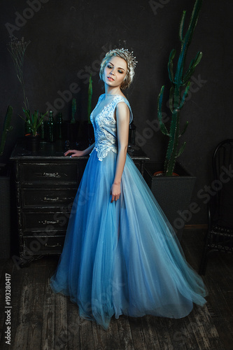 Beautiful model wearing light blue dress is posing in a studio 