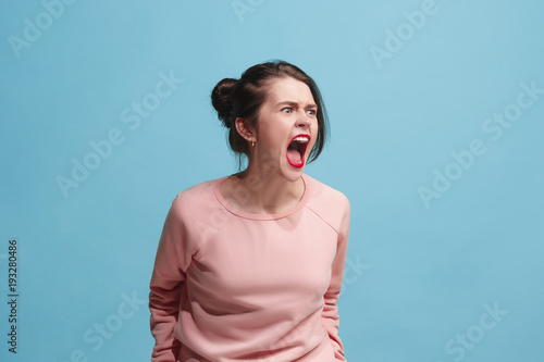 The young emotional angry woman screaming on blue studio background photo