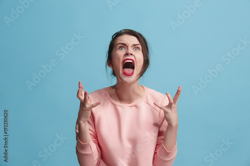 Print op canvas The young emotional angry woman screaming on blue studio background