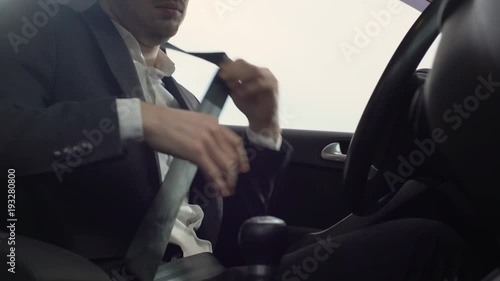 Portrait closeup of caucasian adult man in business suit wearing seat belt for safety, while driving his car on road during afternoon