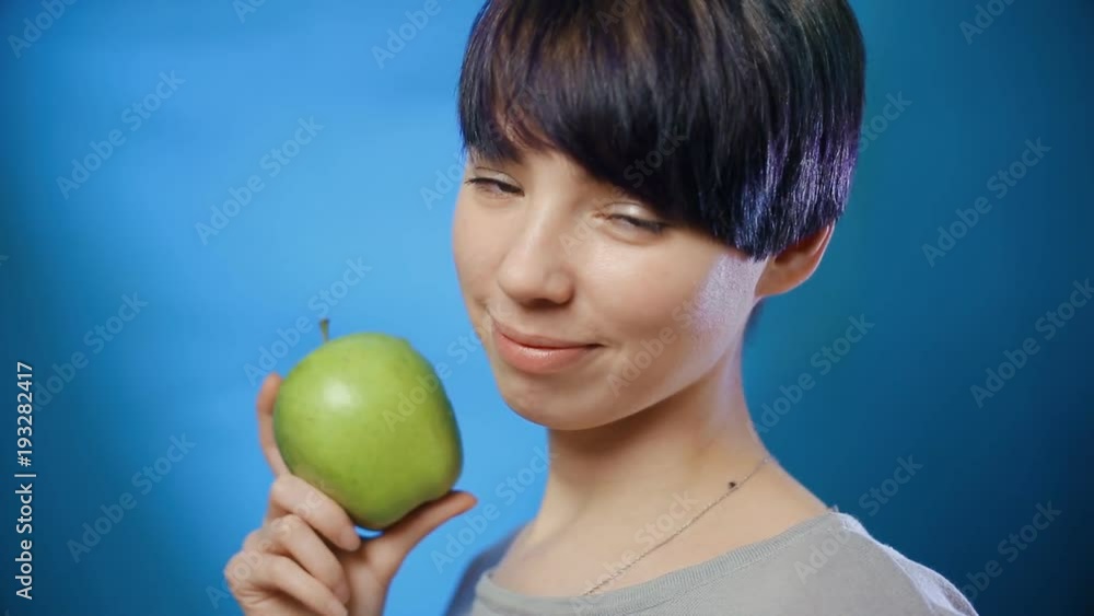 Attractive brunette girl holding a green apple and laughing on a blue wall. Close up Attractive brunette girl holding a green apple and laughing on a blue wall. Close up