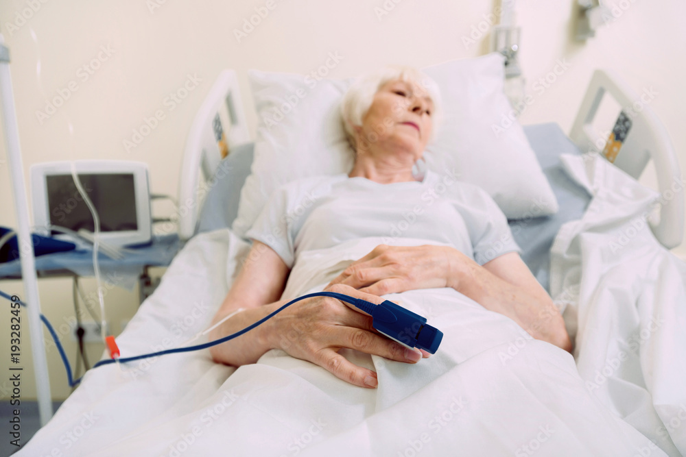 Everything will be alright. Selective focus on a hand of a physically exhausted retired woman thinking about something serious while lying gin a hospital bed with a pulse oximeter on her finger. Everything will be alright. Selective focus on a hand of a physically exhausted retired woman thinking about something serious while lying gin a hospital bed with a pulse oximeter on her finger.