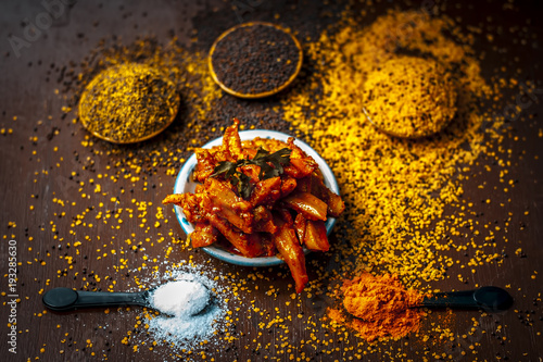 Close up of popular Indian cucumber pickle with all its ingredients including spices and herbs on a wooden surface in dark Gothic colors. photo