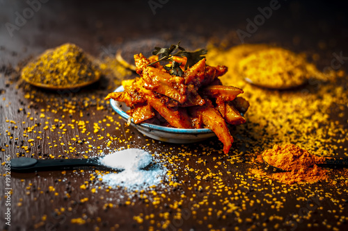 Close up of popular Indian cucumber pickle with all its ingredients including spices and herbs on a wooden surface in dark Gothic colors. photo