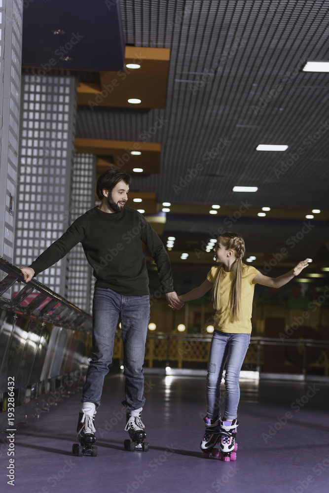 father and daughter holding hands while skating together on roller rink