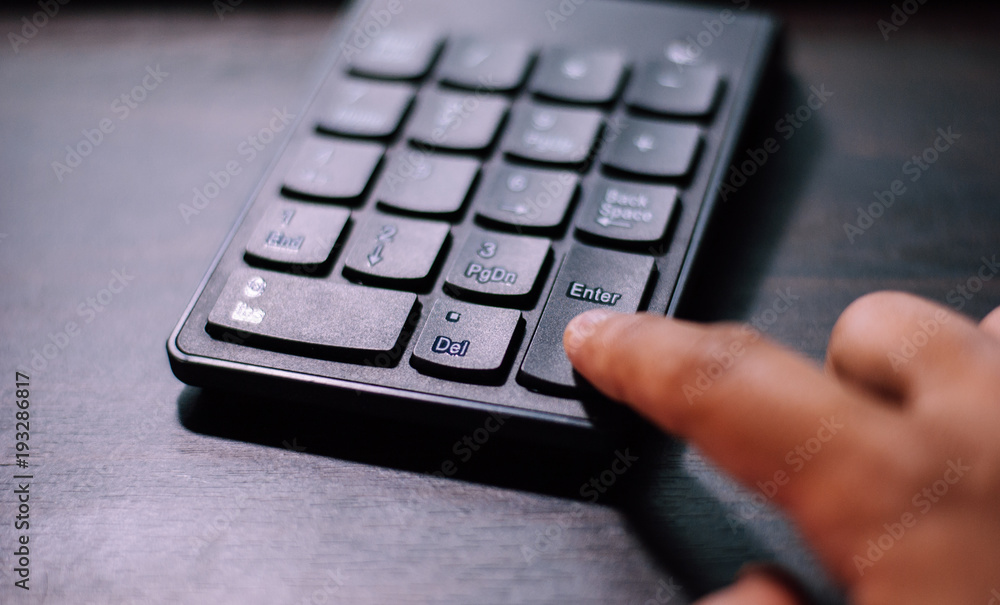 An index finger is pressing on enter button of a black plastic numeral keypad in order to make decision of something very important An index finger is pressing on enter button of a black plastic numeral keypad in order to make decision of something very important