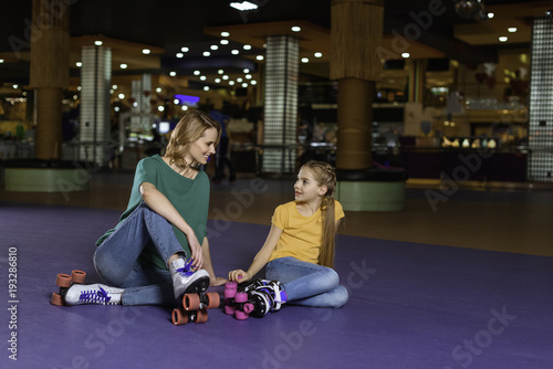 mother and little daughter sitting on roller rink together