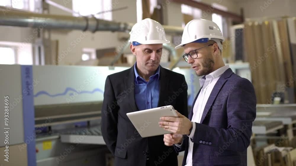 Two adult male executive manager and director discussing process of work on furniture manufacture, while watching in digital tablet slow motion Two adult male executive manager and director discussing process of work on furniture manufacture, while watching in digital tablet slow motion