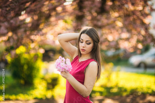 Young girl posing for a photo. Flowering pink trees in the background. Spring. Sakura