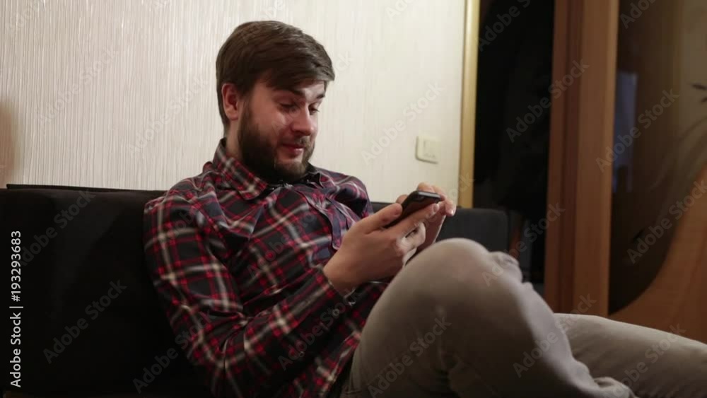 man with a beard sits on the couch and looks into a smartphone man with a beard sits on the couch and looks into a smartphone