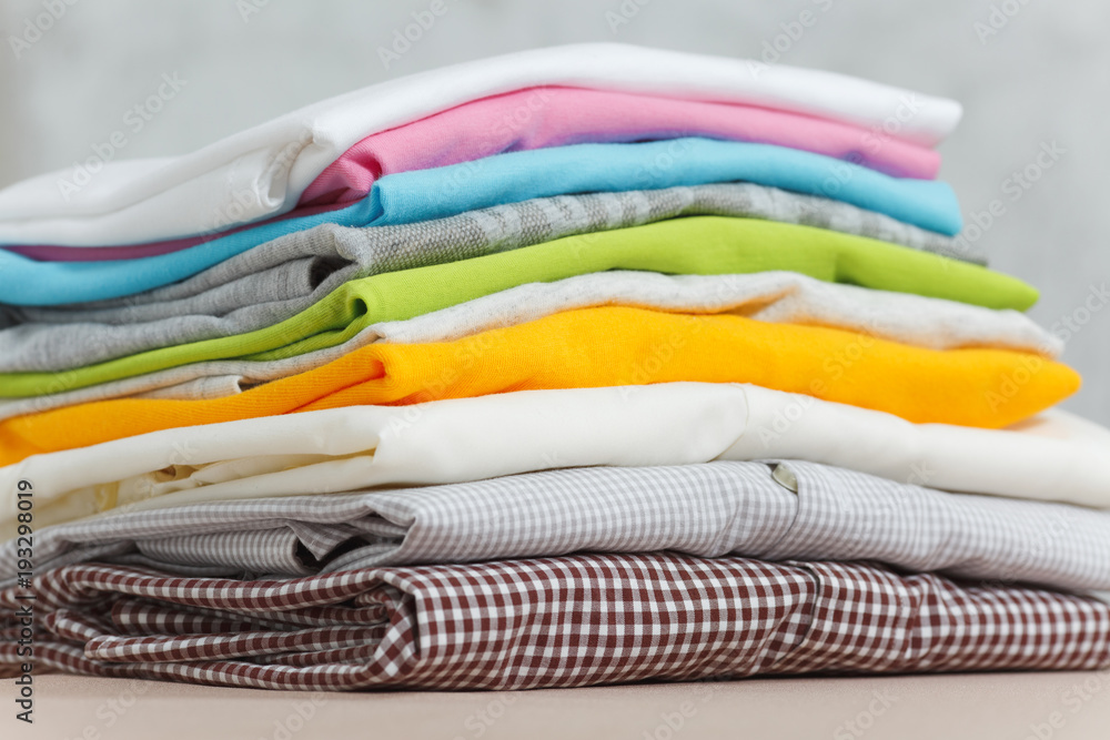 Close up pile of ironing colorful clothes, washed laundry, family clothing on ironing board isolated on white background. Housekeeping concept. Copy space for advertisement. With place for text. Close up pile of ironing colorful clothes, washed laundry, family clothing on ironing board isolated on white background. Housekeeping concept. Copy space for advertisement. With place for text.