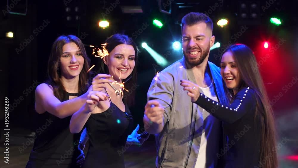 Portrait of four cheerful friends with sparklers on a background of flashing lights. Slow motion. Portrait of four cheerful friends with sparklers on a background of flashing lights. Slow motion.