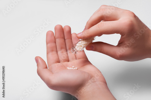 Man's hands pouring a dose of homeopathic pills on white background photo