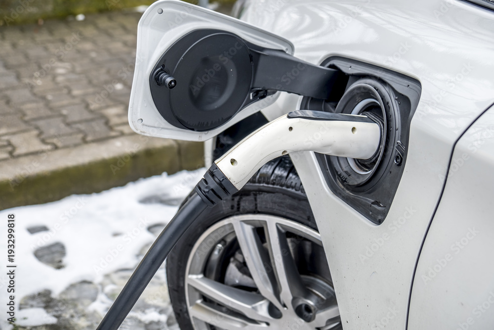 View of an Electric Car Charging and in the background a partial view of a car View of an Electric Car Charging and in the background a partial view of a car