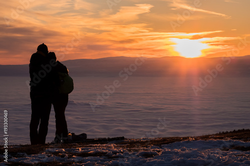 Fotografie Couple on mountain looking over low stratus to beautiful sunset