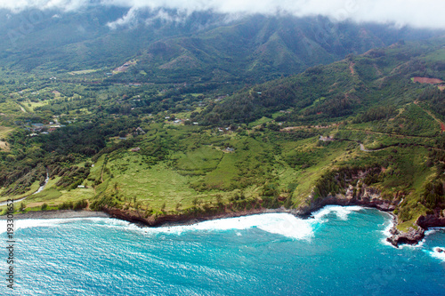 Aerial view of Maui's coastline shows everything from Pacific surf to green fields to mountains and clouds, shot from a small, low-flying prop plane