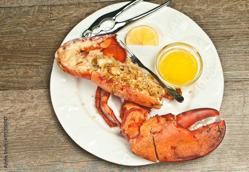 Top view, half, roasted lobster, stuffed, bread crumbs, sliced scallops, on round, white plate, nut cracker and artisan fork slice of lemon and glass bowl of melted butter