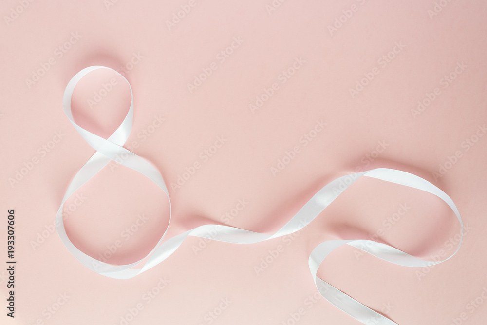 White gift celebration ribbon in 8 digit shape over pink background White gift celebration ribbon in 8 digit shape over pink background