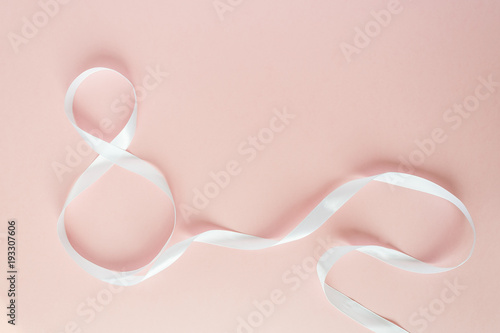 White gift celebration ribbon in 8 digit shape over pink background