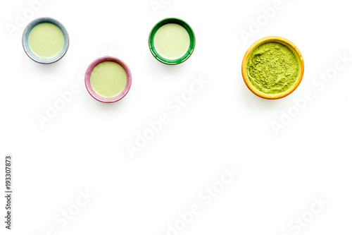 Brew matcha tea. Bowl with powder and cups with beverage on white background top view copy space