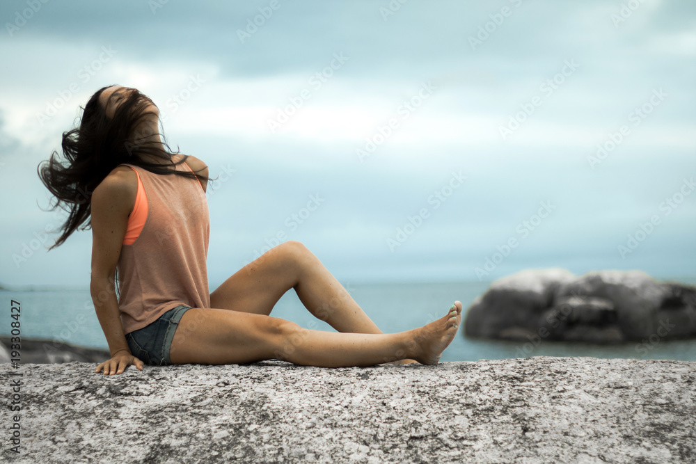 Woman sitting on a rock flicking her hair at sunset on Bakovern Beach, Cape Town. Woman sitting on a rock flicking her hair at sunset on Bakovern Beach, Cape Town.