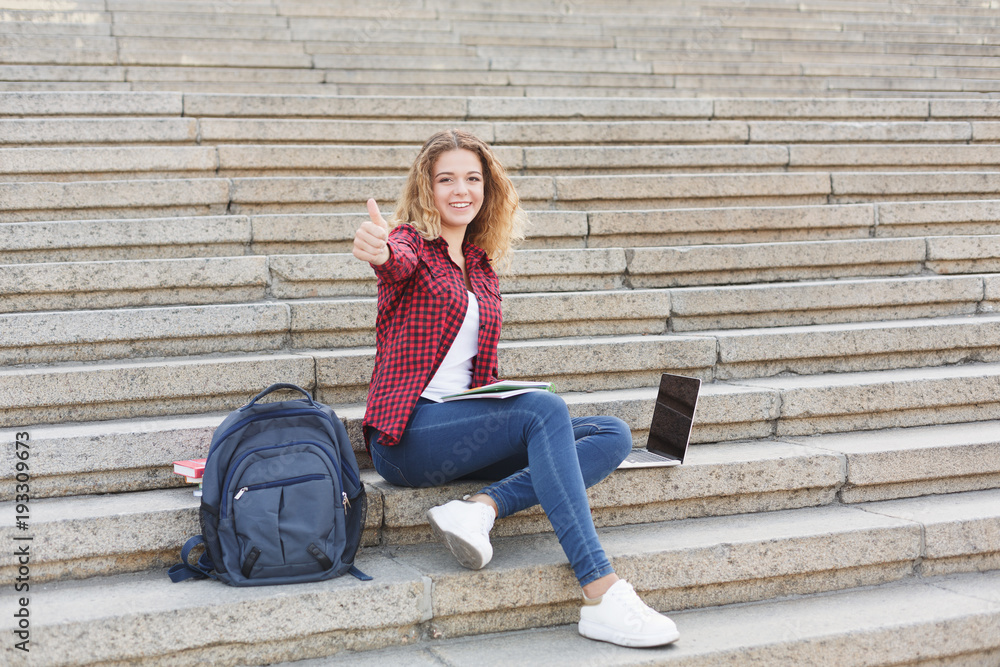 Smiling female student sitting on the stairs using laptop outdoors Smiling female student sitting on the stairs using laptop outdoors