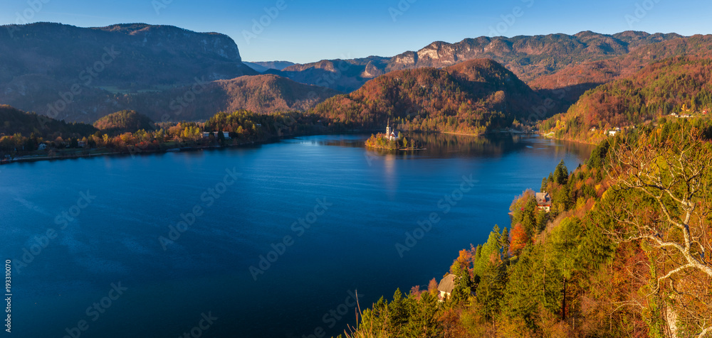 Bled, Slovenia - Panoramic skyline view of Lake Bled with warm autumn foliage and the famous Pilgrimage Church of the Assumption of Maria and the Alps at background