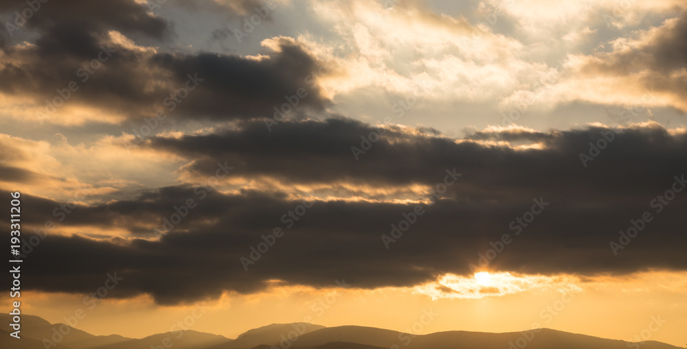 Sunrise or sunset over mountains silhouette. Sunbeams come through the colorful clouds. Space, banner.