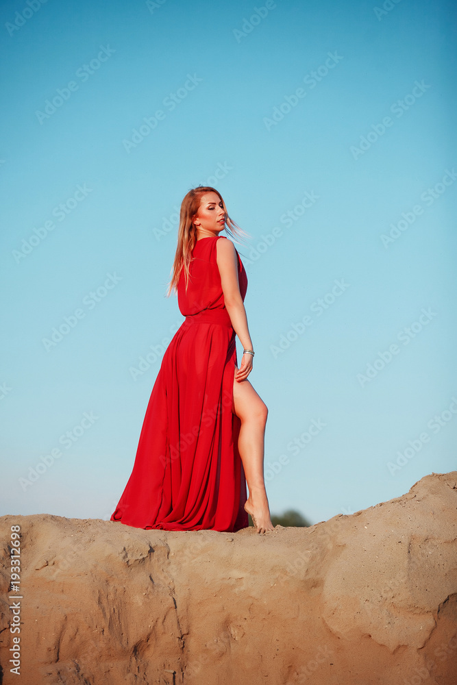 Woman dancing on sunset in red long dress on the beach on blue sky backgound