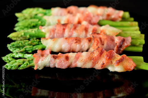 Green asparagus wrapped into smoked bacon on a black plate