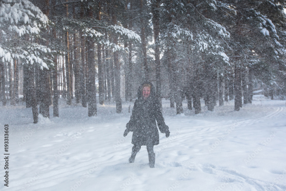 Naklejka premium Young woman in the forest in a strong snowstorm.
