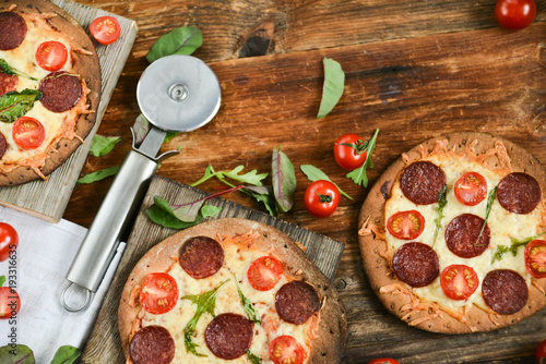 Mini Pizza With Cherry Tomatoes And Salami Sausages On A Wooden Background Natural Rustic, A Pizza Cutter And Ingridienty. photo