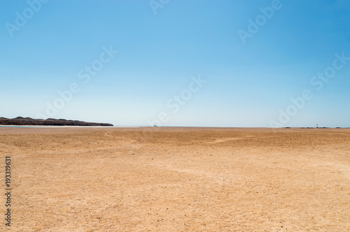 deserted seashore, with yachts and a lighthouse in the background, against a blue sky background