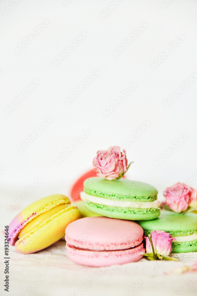 Dessert: A Delicate Fresh Colorful French Macaroons In Pastel Colors With Flowers Roses On A Light Textile Background, Top View Dessert: A Delicate Fresh Colorful French Macaroons In Pastel Colors With Flowers Roses On A Light Textile Background, Top View