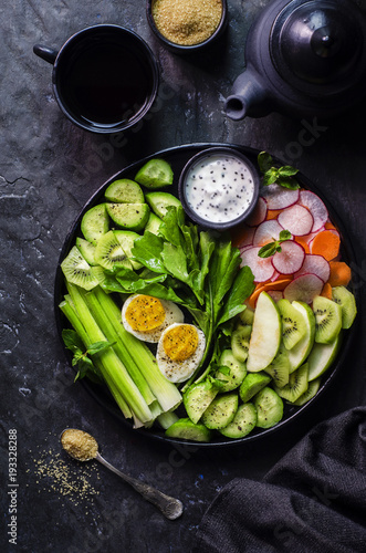 Healthy salad with fresh cucumber,celery,watercress,carrot,radish,green apple,kiwi and boiled egg on black plate.Top view,close-up