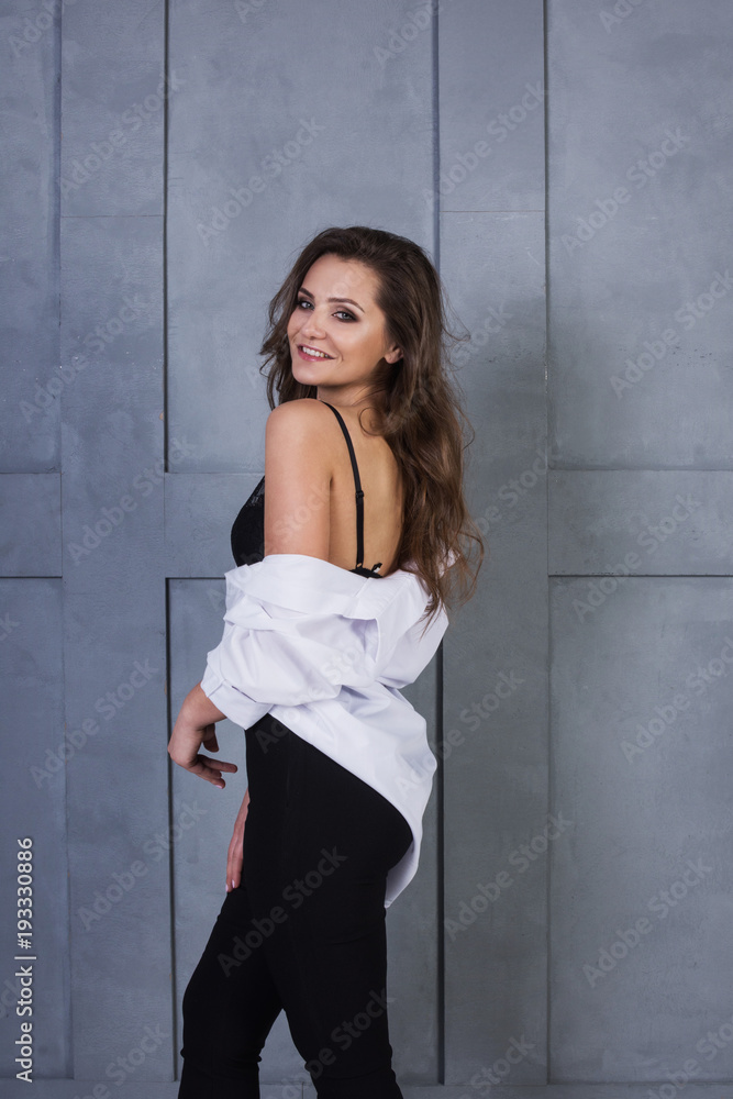 Portrait of a young smiling woman on a gray wall background. A beautiful girl in white shirt and black lingerie stands near a concrete wall Portrait of a young smiling woman on a gray wall background. A beautiful girl in white shirt and black lingerie stands near a concrete wall